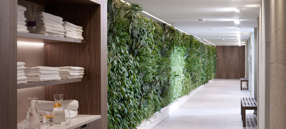 Eleganter Korridor im Spa-Bereich des Hotels Giardino Marling mit einer grünen Wand mit Pflanzen; links ein Regal mit gefalteten Handtüchern