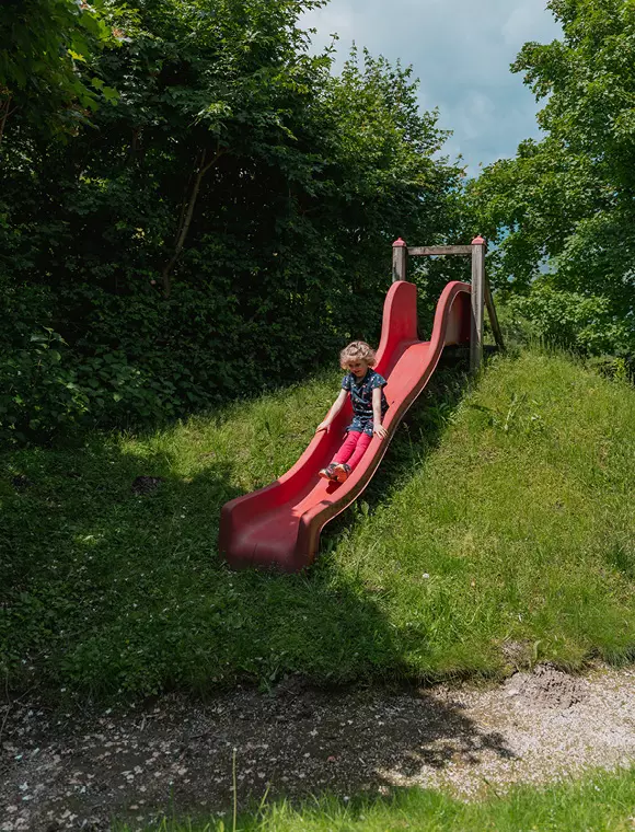 Mädchen rutscht auf roter Rutsche im Grünen