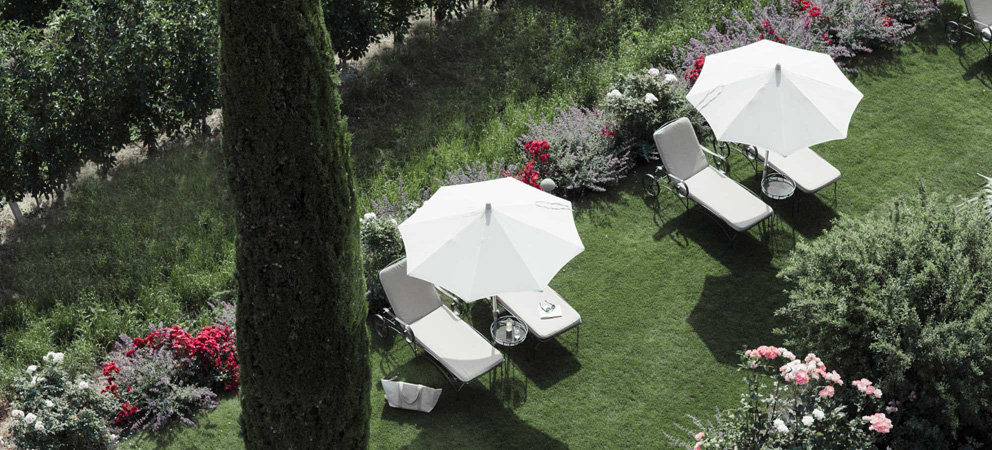 zwei Paar Liegestühle mit Sonnenschirm im Garten des Giardino Marling von oben gesehen