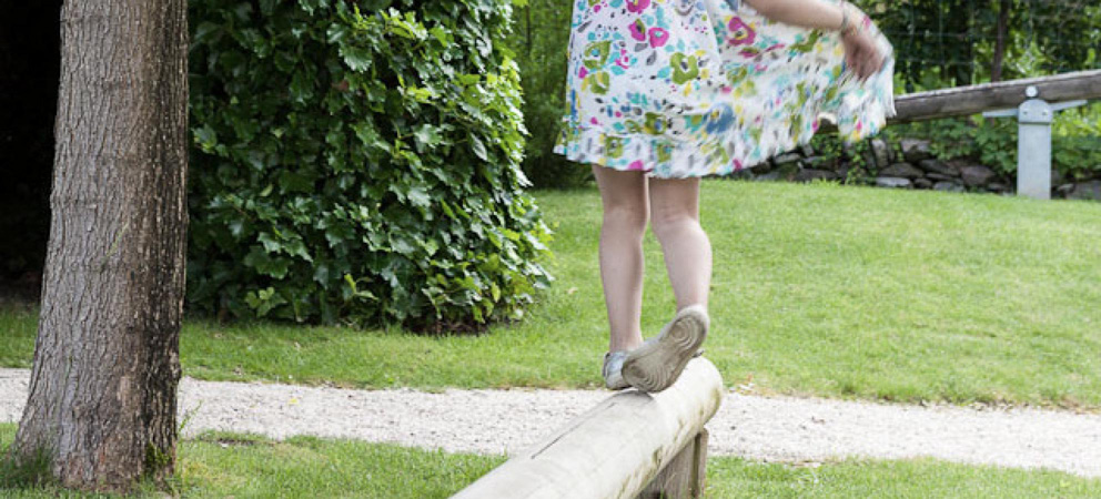 une petite fille en équilibre sur une poutre en bois dans la cour de récréation du Giardino Marling