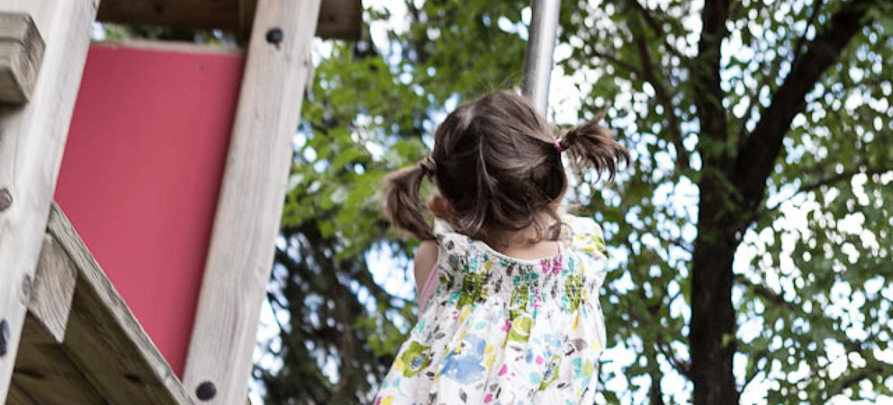 ein kleines Mädchen klettert auf eine Metallstange auf dem Kinderspielplatz des Giardino Marling