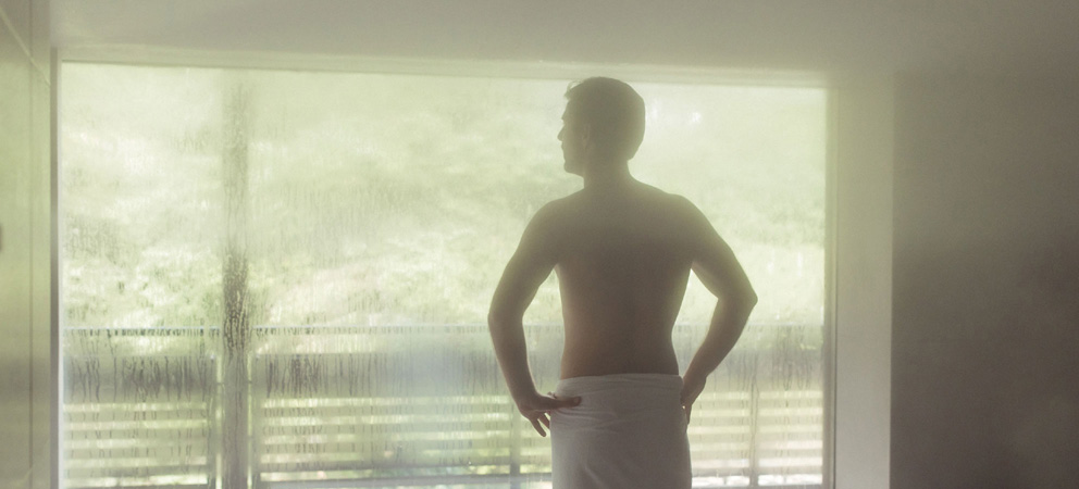 a young man is standing topless in the spa of the Giardino Marling with a towel around his waist