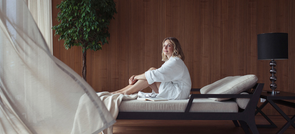 una giovane donna bionda in accappatoio siede su un letto nella zona relax della Spa del Giardino Marling