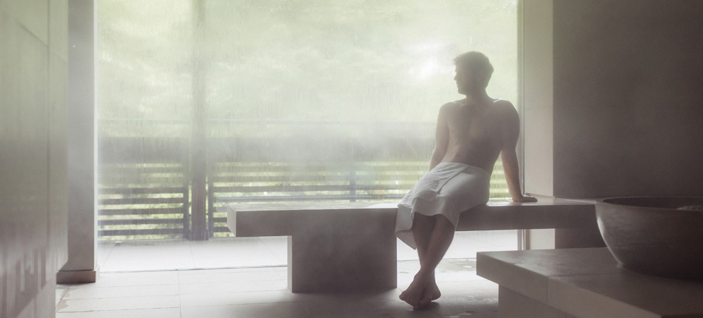 un giovane uomo con solo un asciugamano intorno alla vita si siede nel bagno di vapore del Giardino Marling