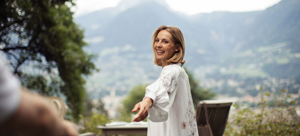 A lady with her hand outstretched towards the camera, the mountains of Merano in the background